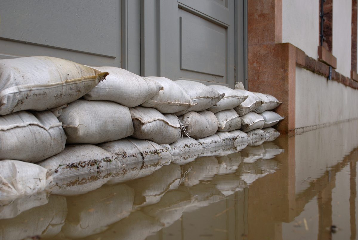 Sandbags stacked across a doorway, with floodwater reflecting the wall behind them