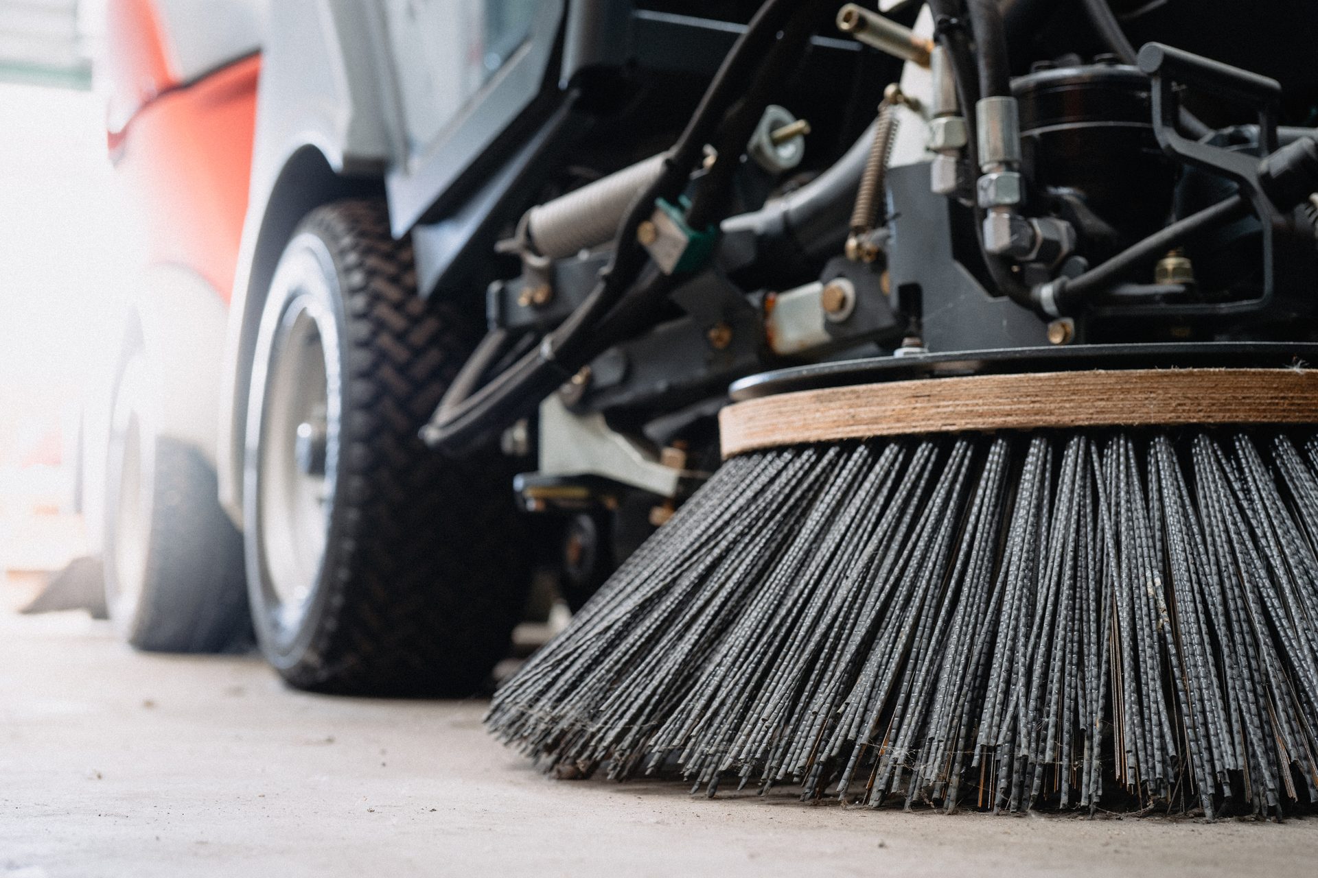 A close-up of the rotating side brush and front wheel of a street sweeper on concrete